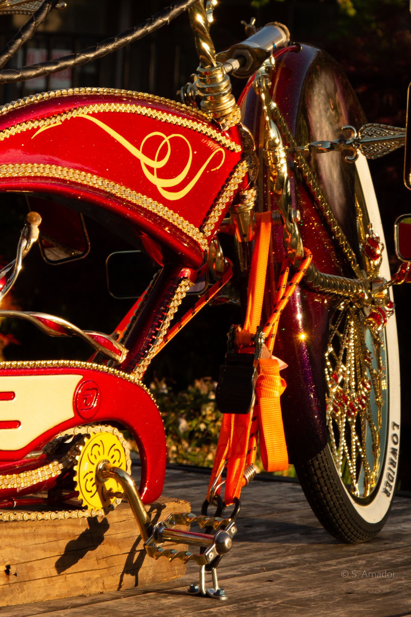 Ornate red and gold decorated lowrider bicycle with beads in warm sunset golden light.