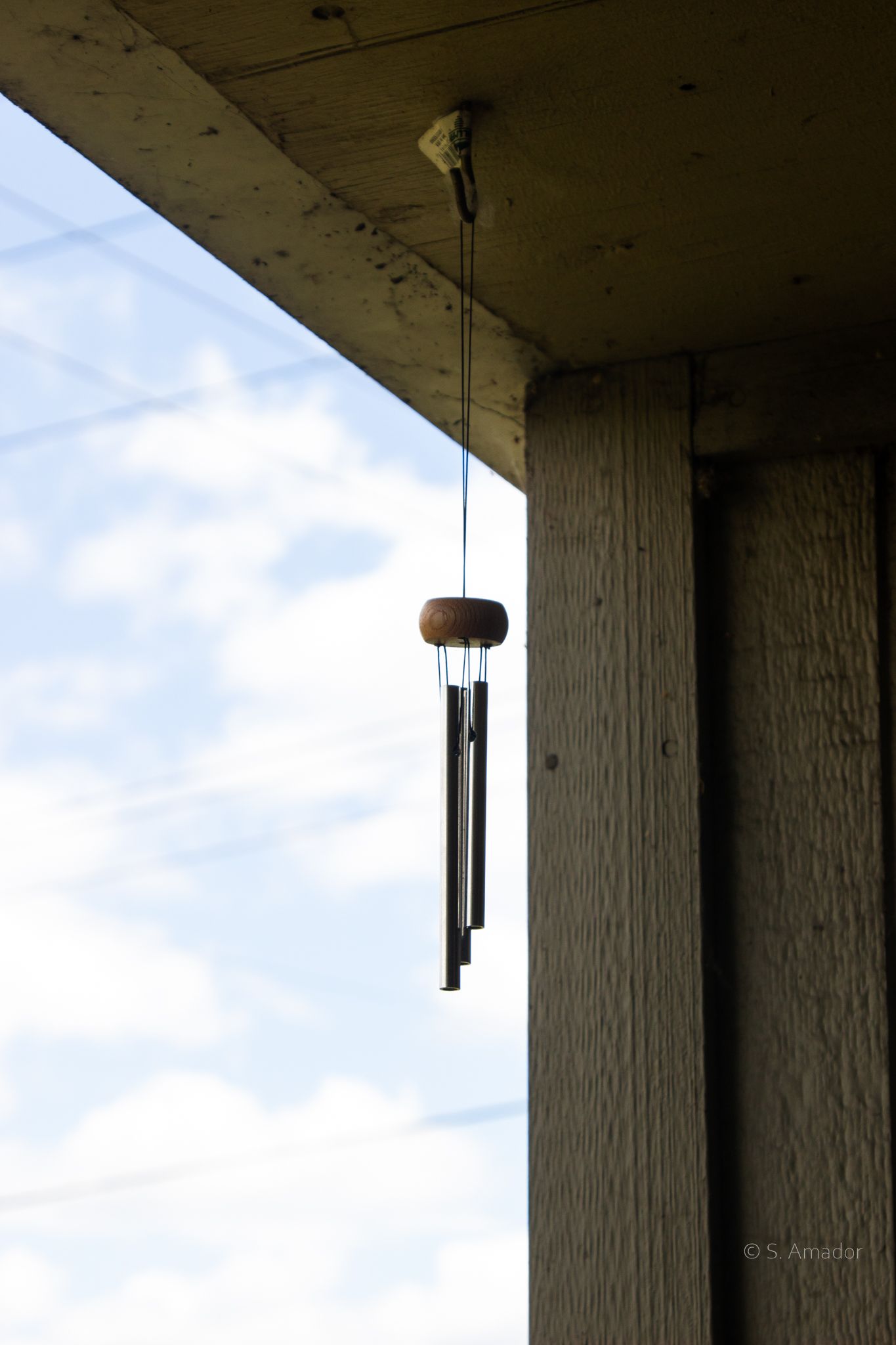 Wind chimes hanging from a wooden porch ceiling against a cloudy blue sky.