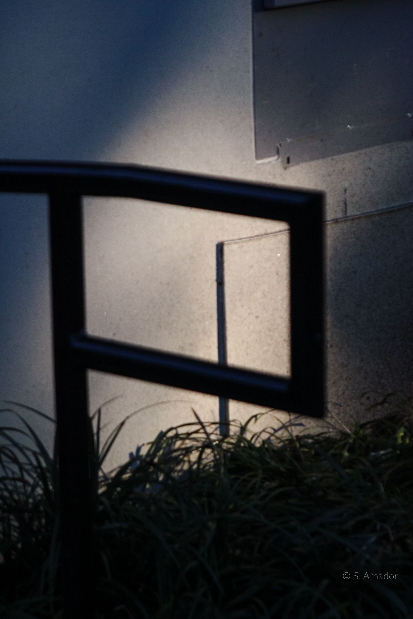 Shadow of metal railing casting geometric rectangle pattern on illuminated concrete wall at dusk.
