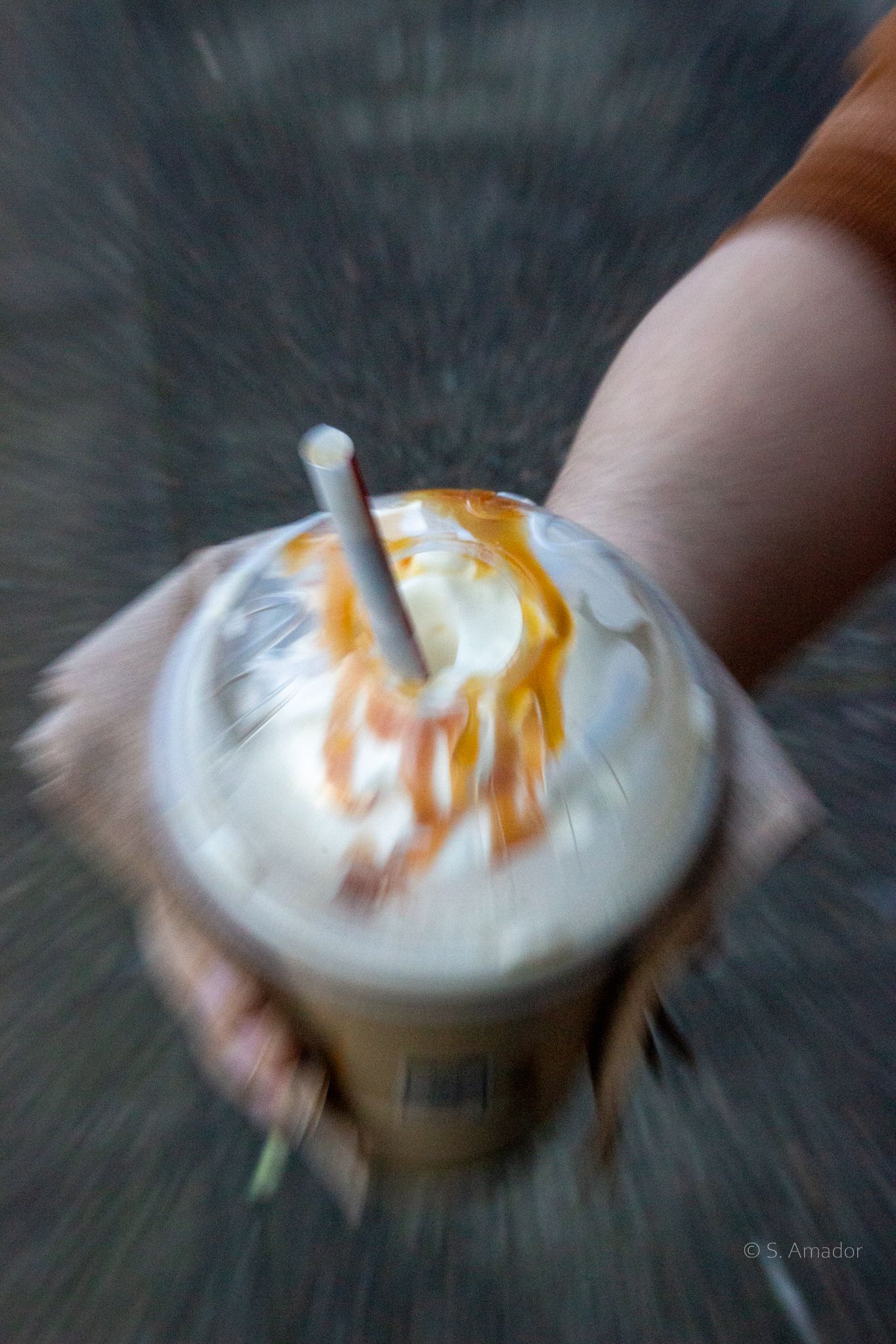 Hand holding a caramel drizzled iced coffee drink with whipped cream and straw, motion blur effect.