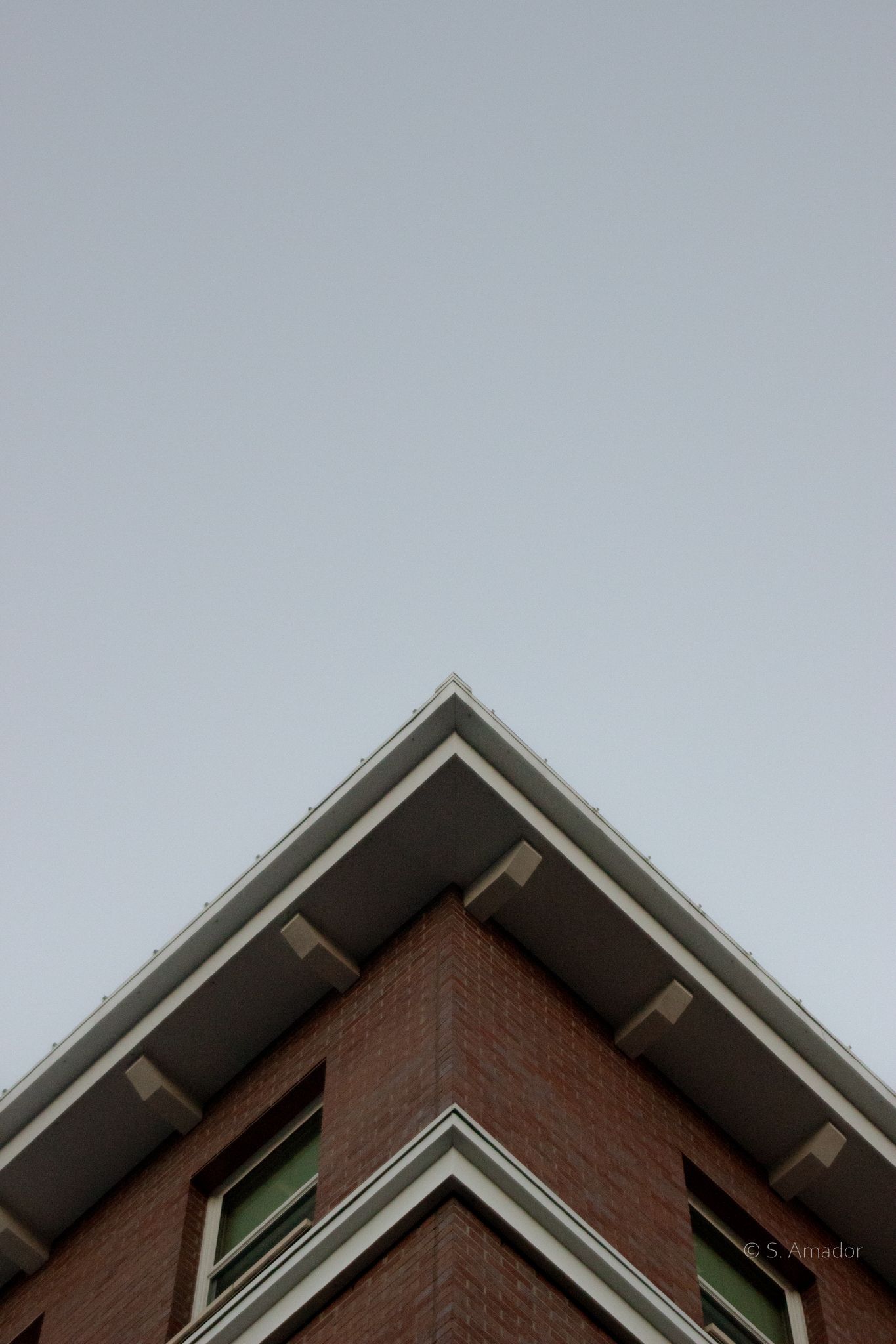 Corner view of a red brick building with white trim roofline against a clear gray sky.