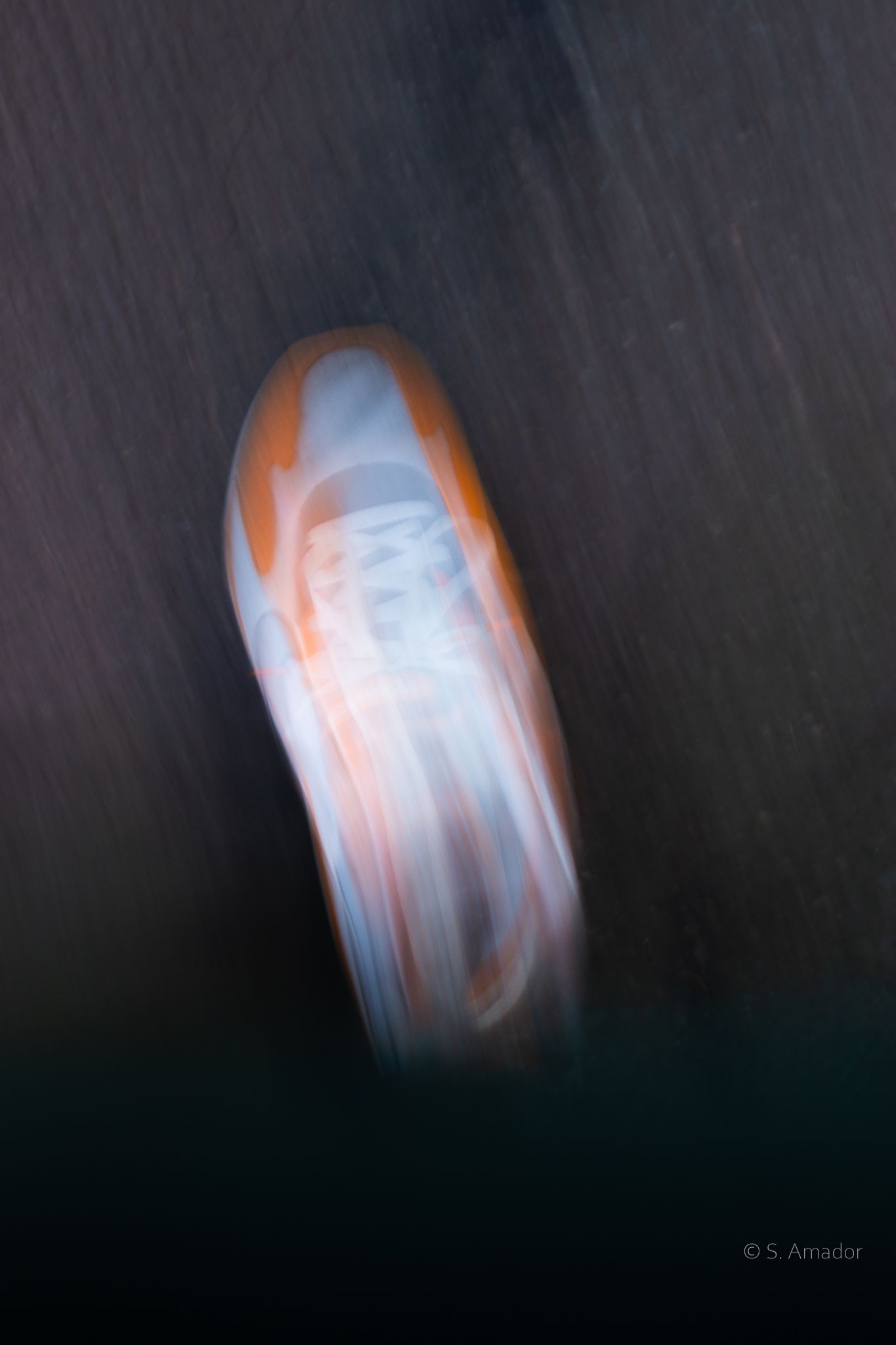 Abstract motion blur photo of a white and orange sneaker shoe in dynamic movement against dark background.