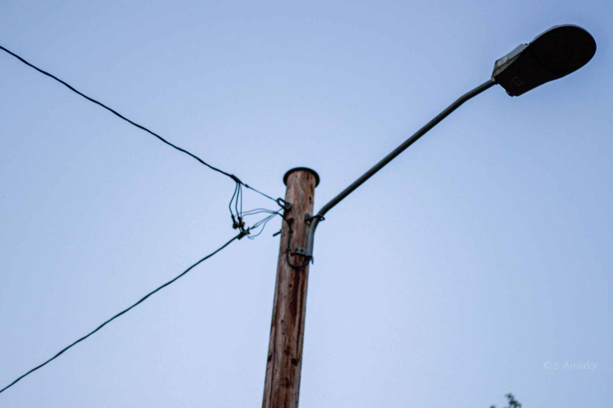 Wooden utility pole with street light arm and power lines against a clear blue sky.