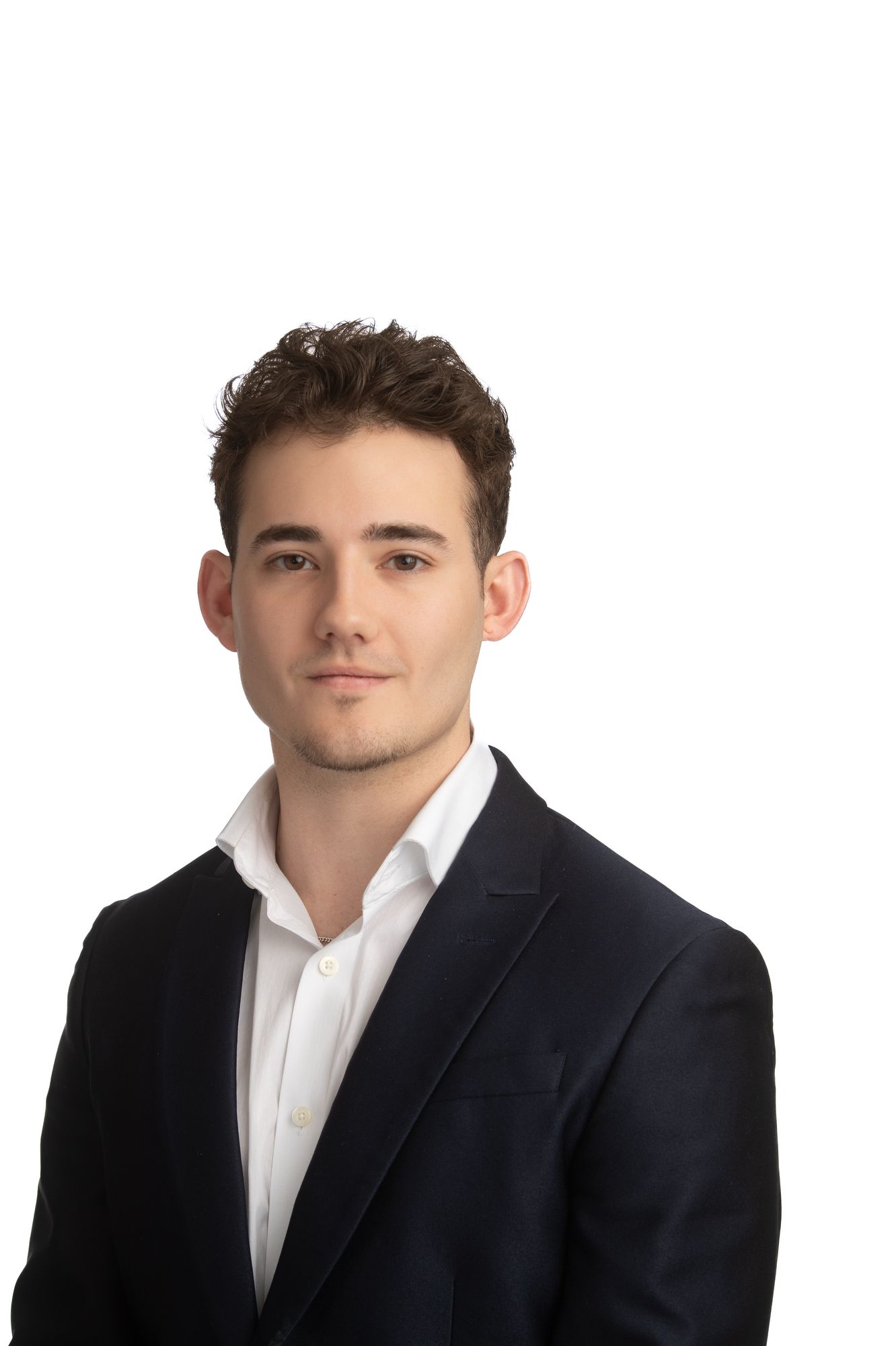 Young professional man in dark blazer and white shirt poses for a formal headshot on white background.