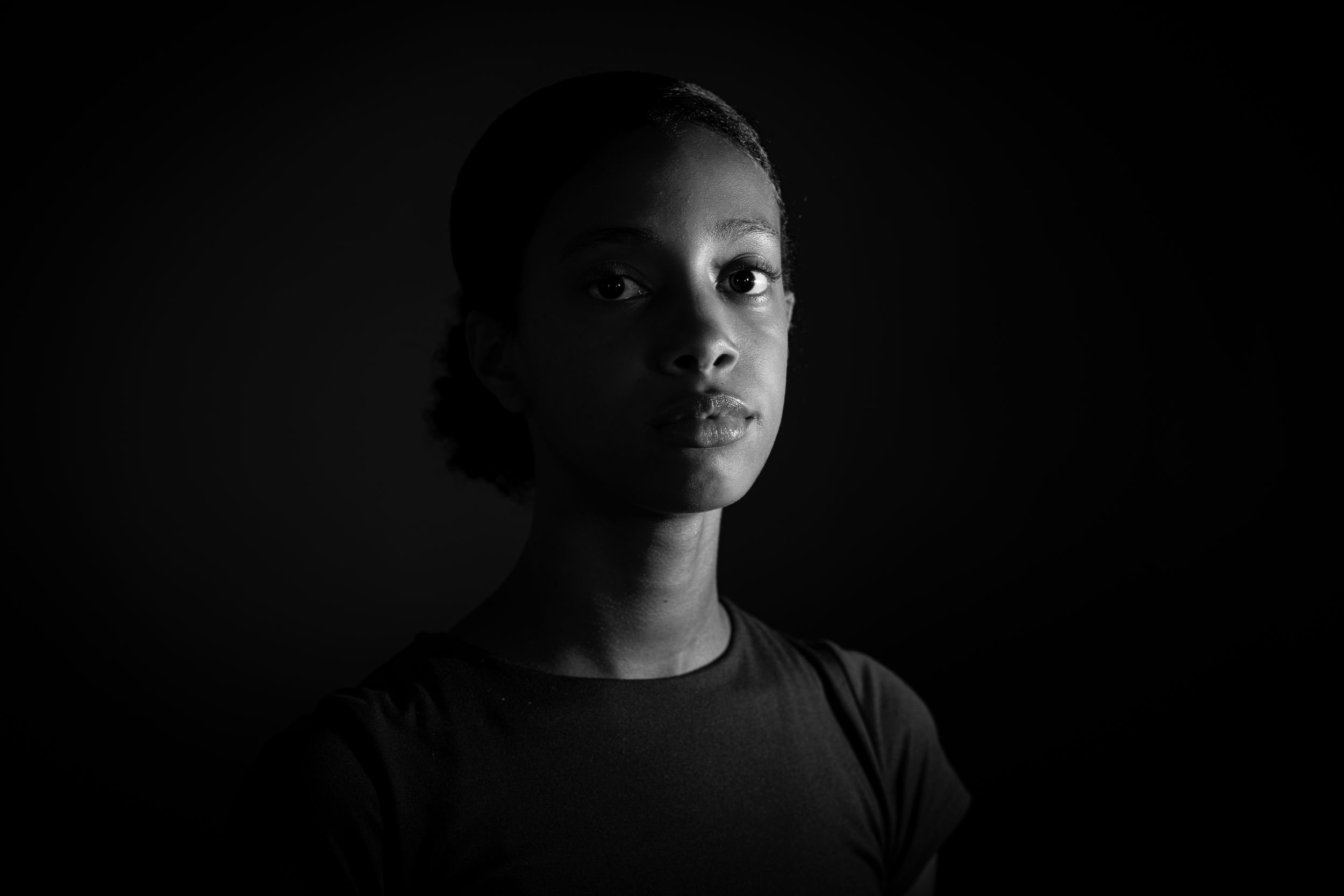 Black and white portrait of a young child looking up against a dark background.