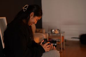Woman in black jacket reviewing photos on a camera in a dimly lit room.