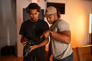 Two men reviewing photos on a camera in a photography studio, one wearing headphones and the other a gray cap.