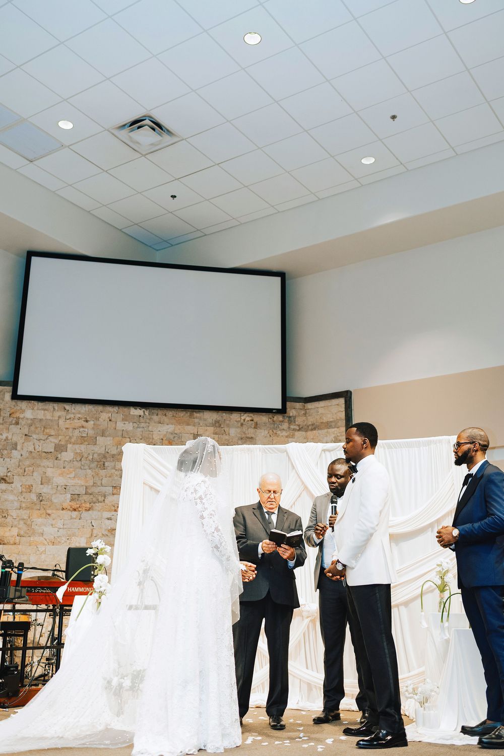 Bride and groom exchanging vows at church altar with officiant and groomsman during elegant wedding ceremony.