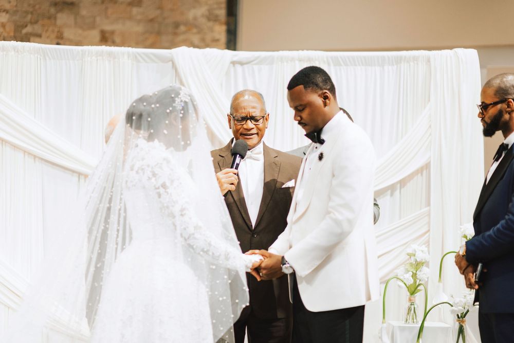 Bride and groom exchange vows at elegant white draped wedding altar with officiant holding microphone.
