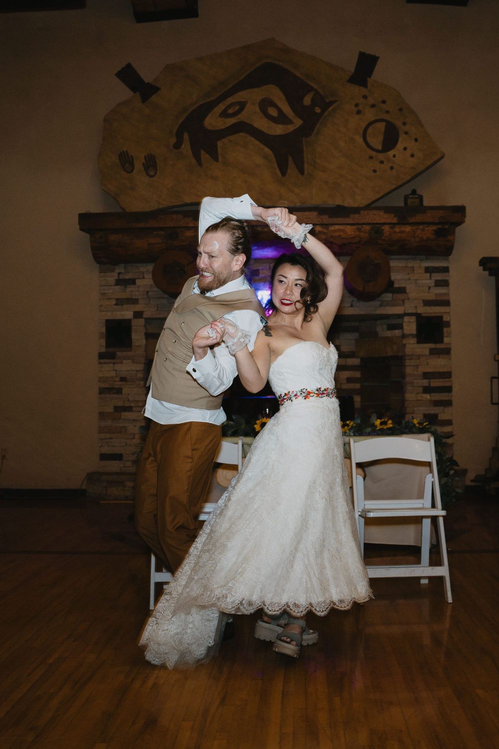 Bride and groom dancing together in front of a rustic stone fireplace at their wedding reception.