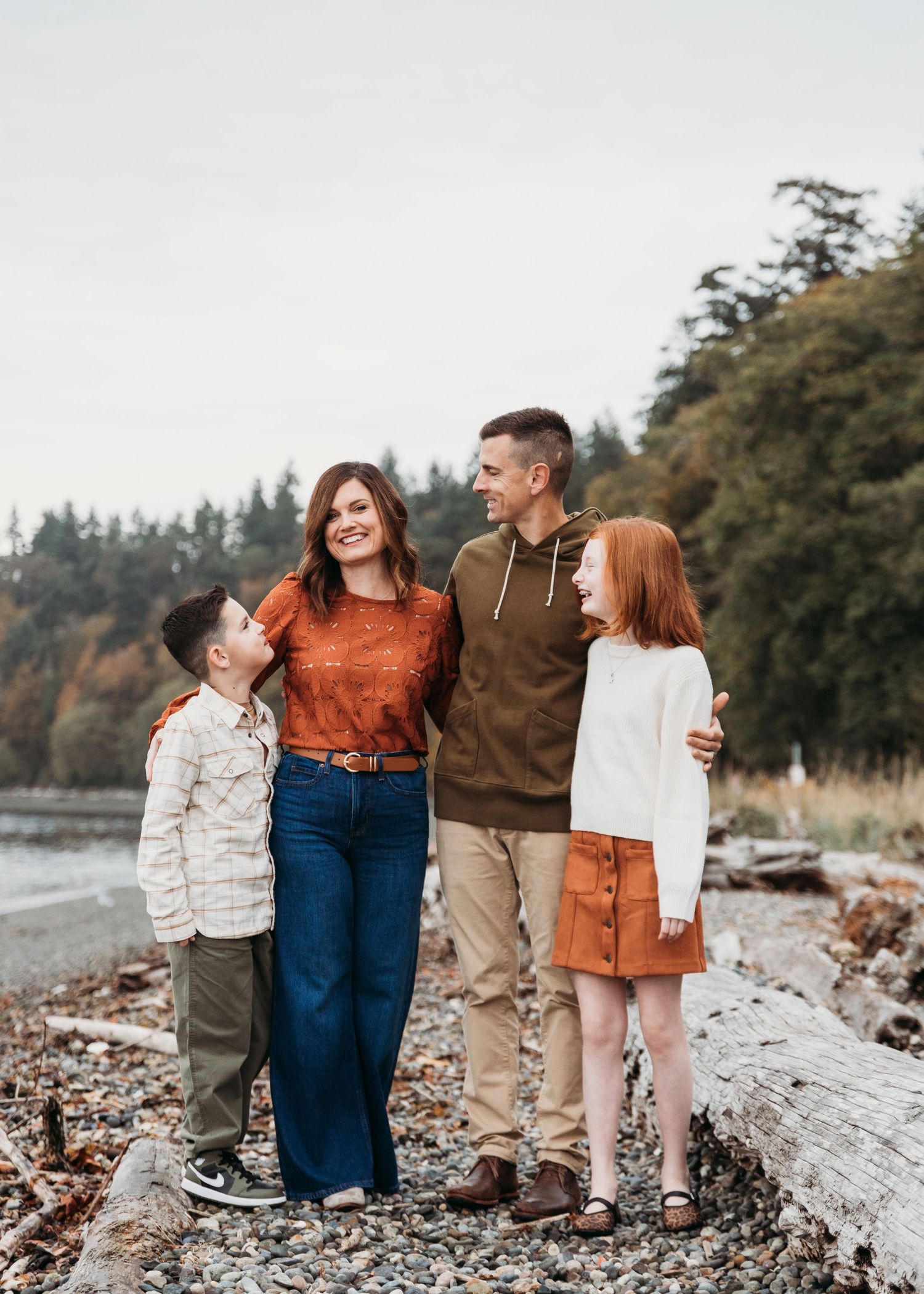 Group in fall casual wear standing on rocky beach with autumn trees in background.