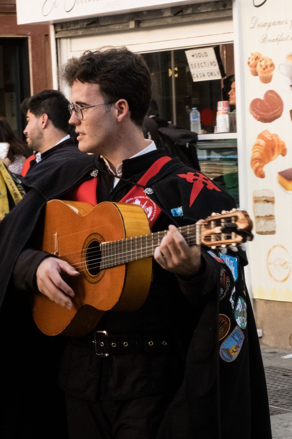 Young male street musician in traditional Spanish tuna costume playing acoustic guitar while marching in a city parade.