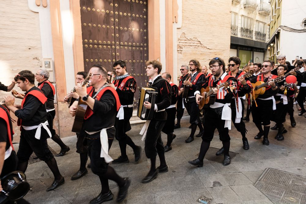 Spanish tuna student musicians in black and red traditional costumes marching in procession through historic city streets.