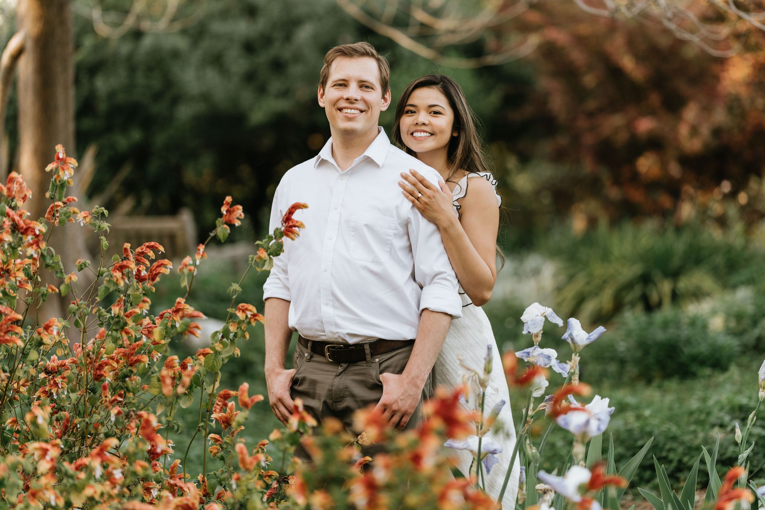 Mariel and Jeff embracing among vibrant seasonal flowers at the Arboretum.