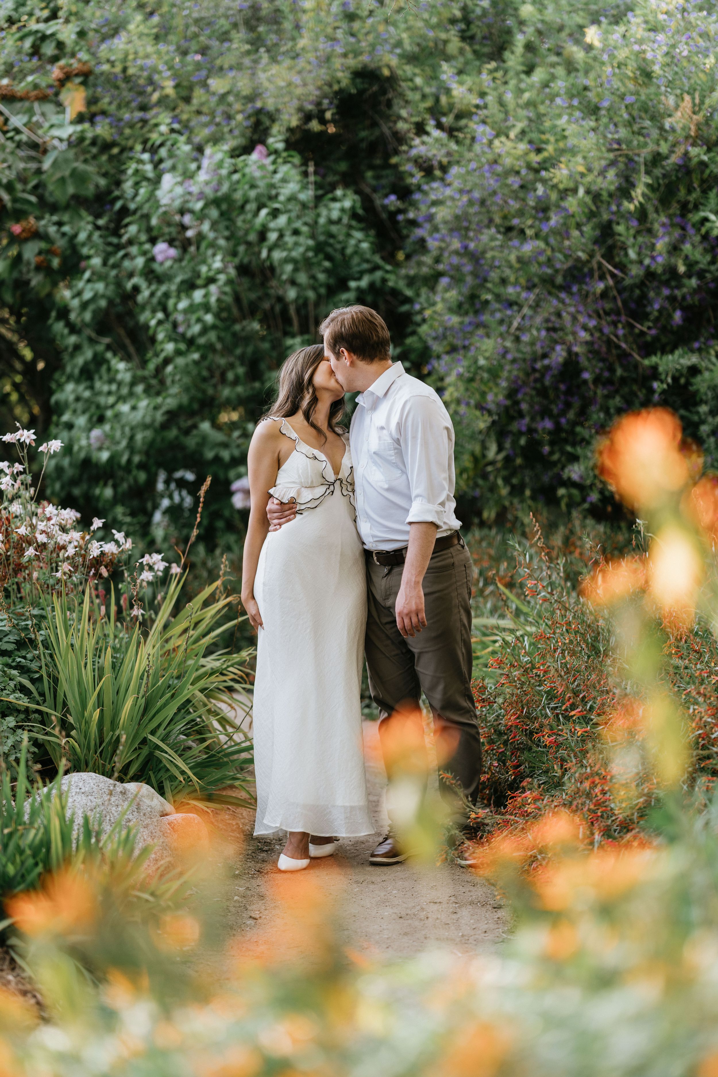Mariel and Jeff sharing a kiss along a garden pathway at the Los Angeles County Arboretum.