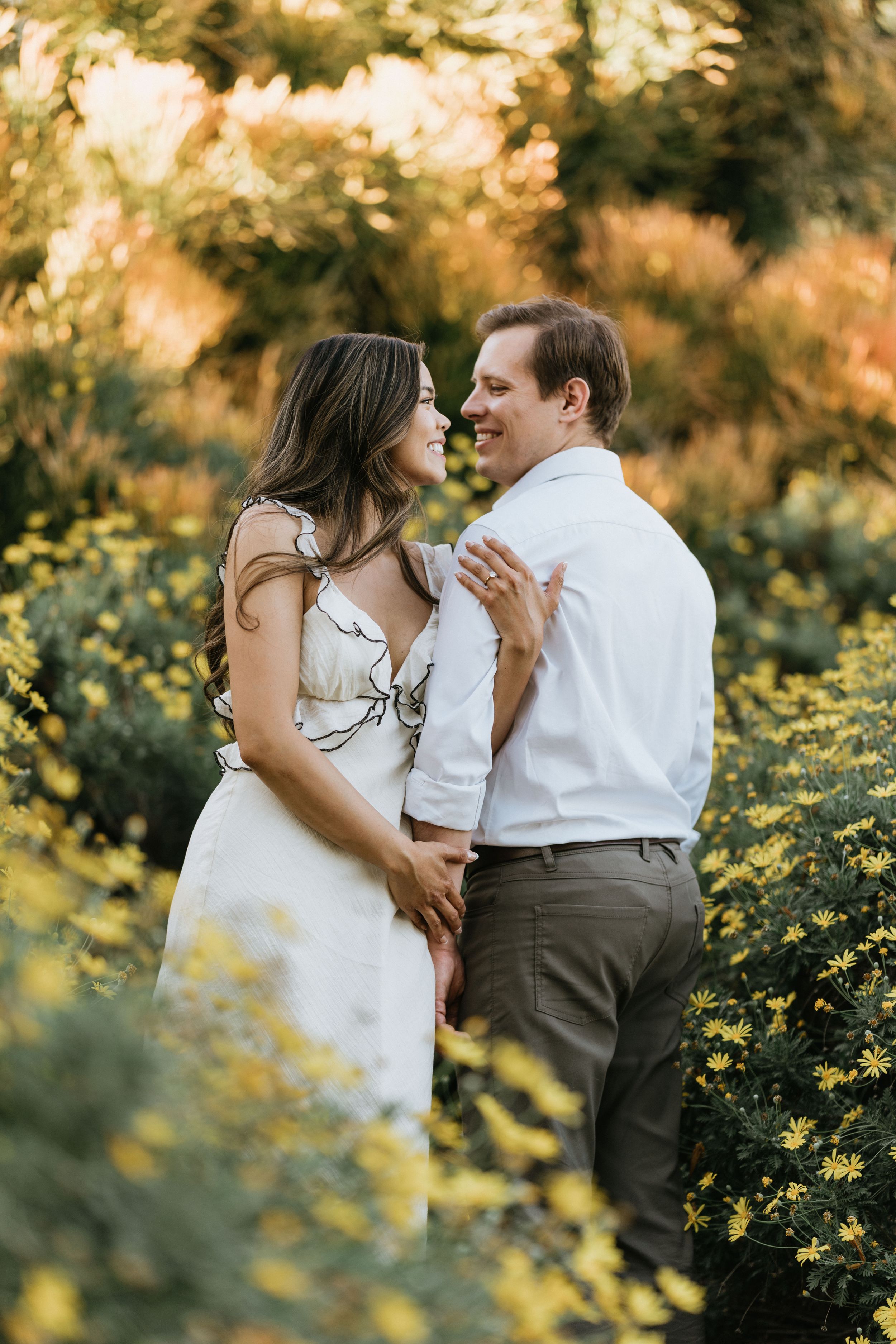 Romantic engagement portrait surrounded by golden light and blooming flowers.