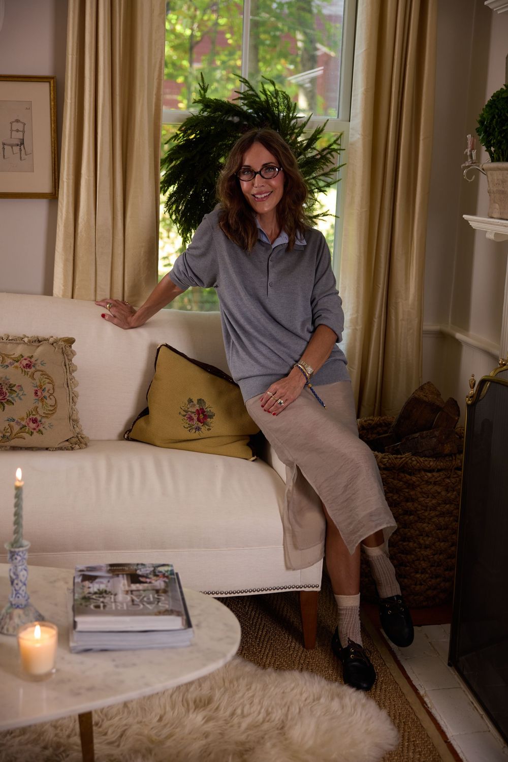 Smiling woman in gray pullover and linen skirt posing on white sofa in cozy living room.