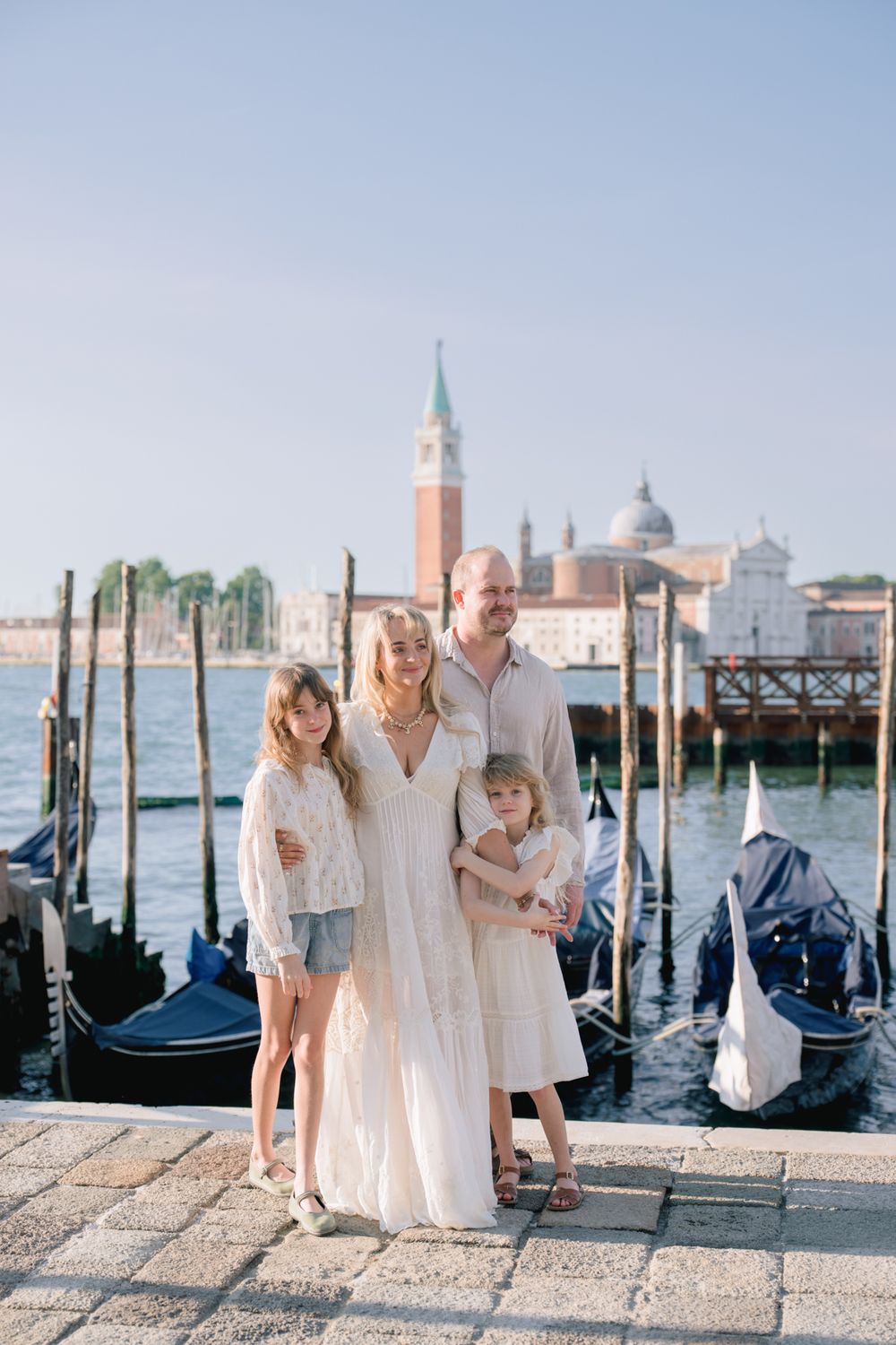 Family of four posing by Venice gondola docks with San Giorgio Maggiore church in background.