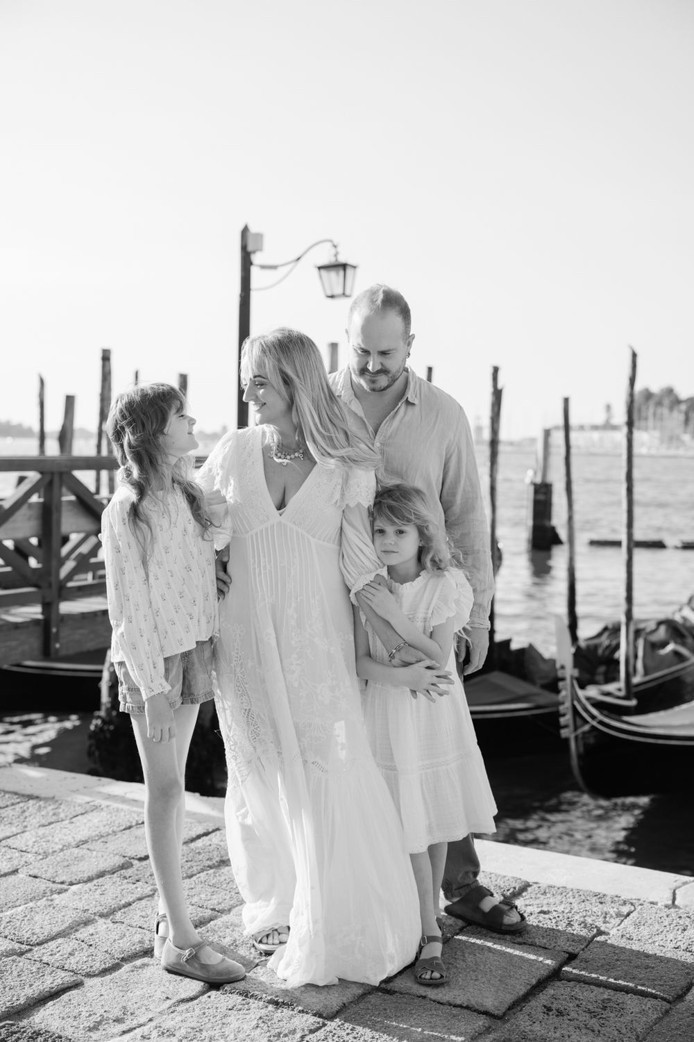 Black and white family portrait of four people posing by Venice gondolas on a sunny day.