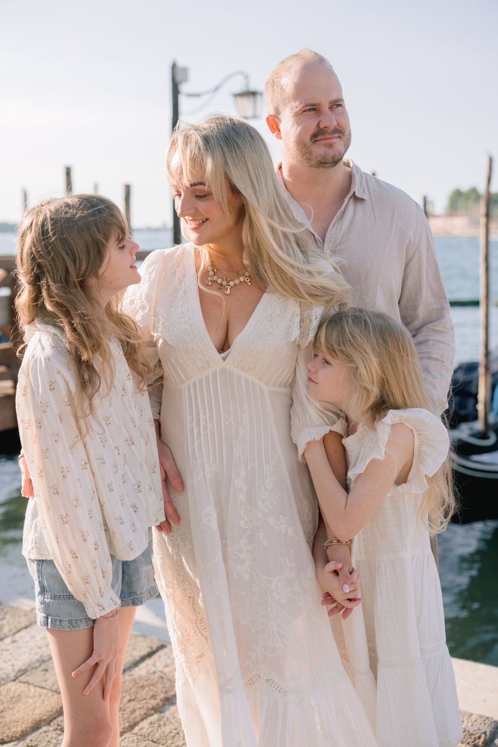 Family of four in cream outfits posing on a Venice dock with gondolas in the background.