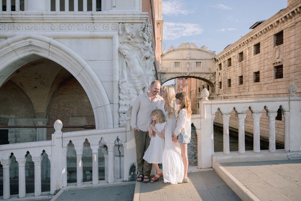 Family posing near the Bridge of Sighs in Venice, Italy, with ornate white stone architecture.