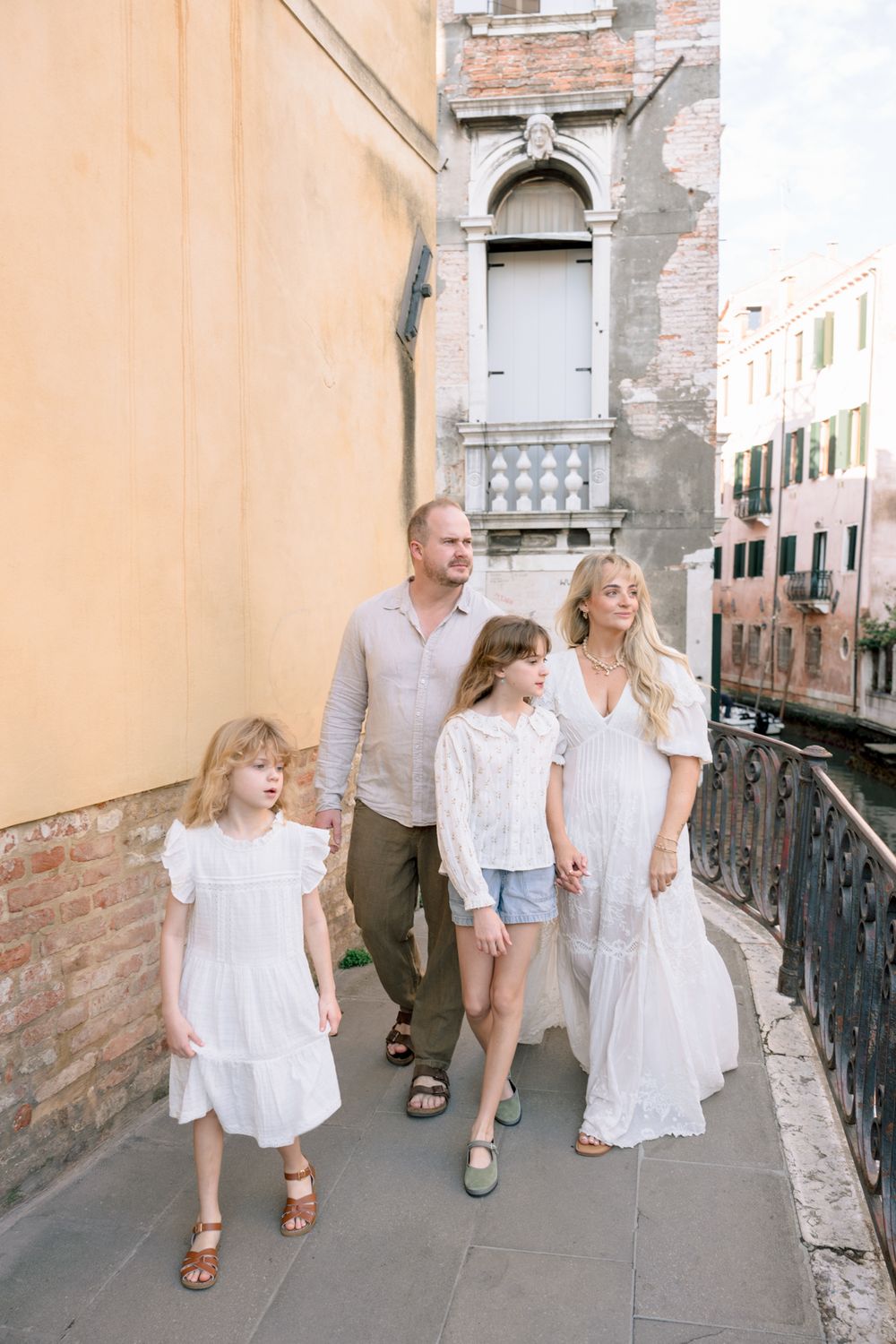 Family of four walking along a scenic Venice canal street in coordinated white outfits.