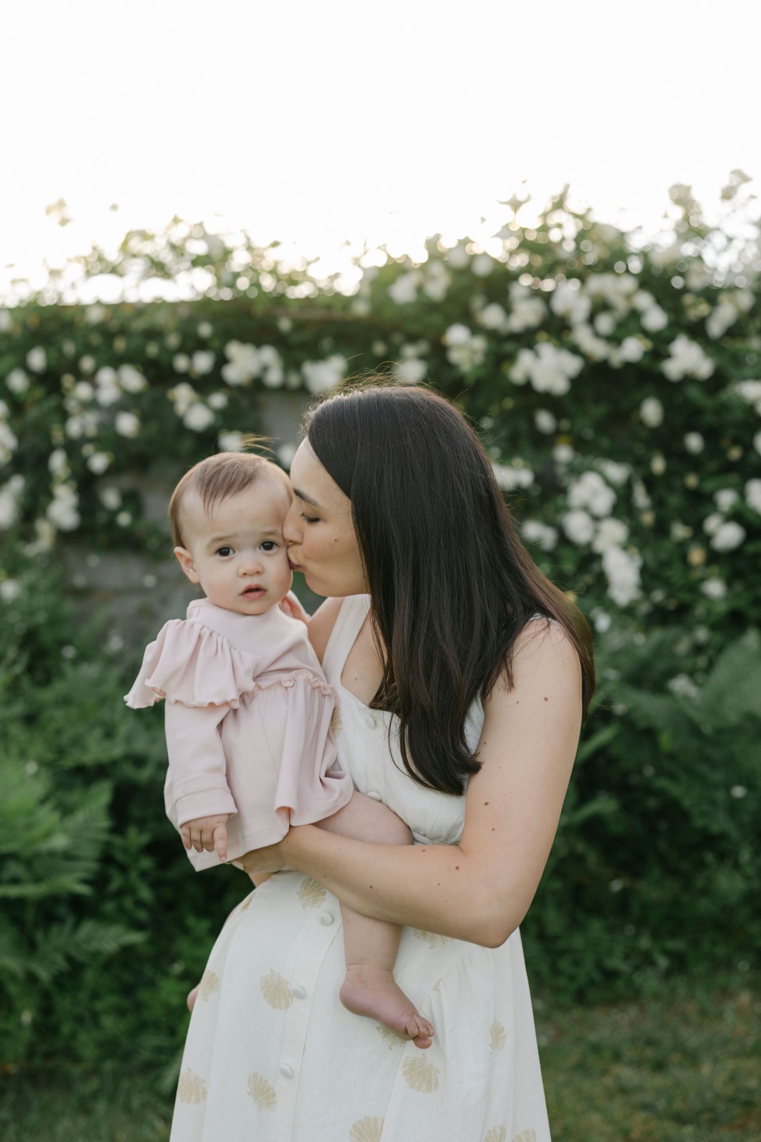 Sweet tender moments between mother and baby in white lace dress against light background.