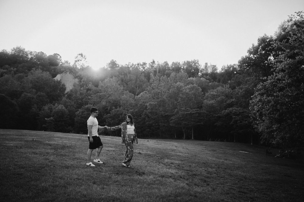 Black and white photo of couple holding hands in a grassy field at sunset.