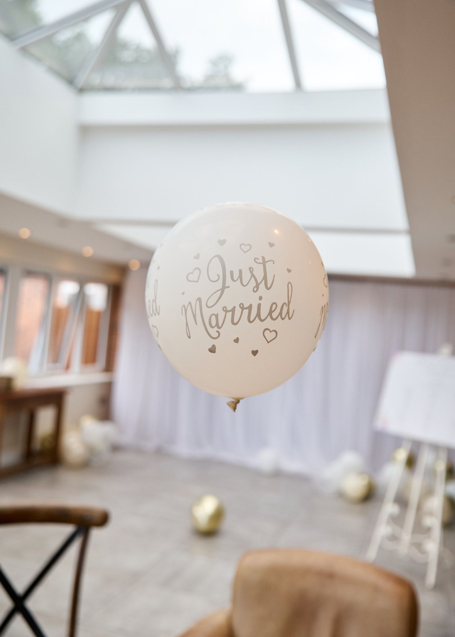 A white "Just Married" balloon with gold text floats in an elegant wedding venue with soft lighting.