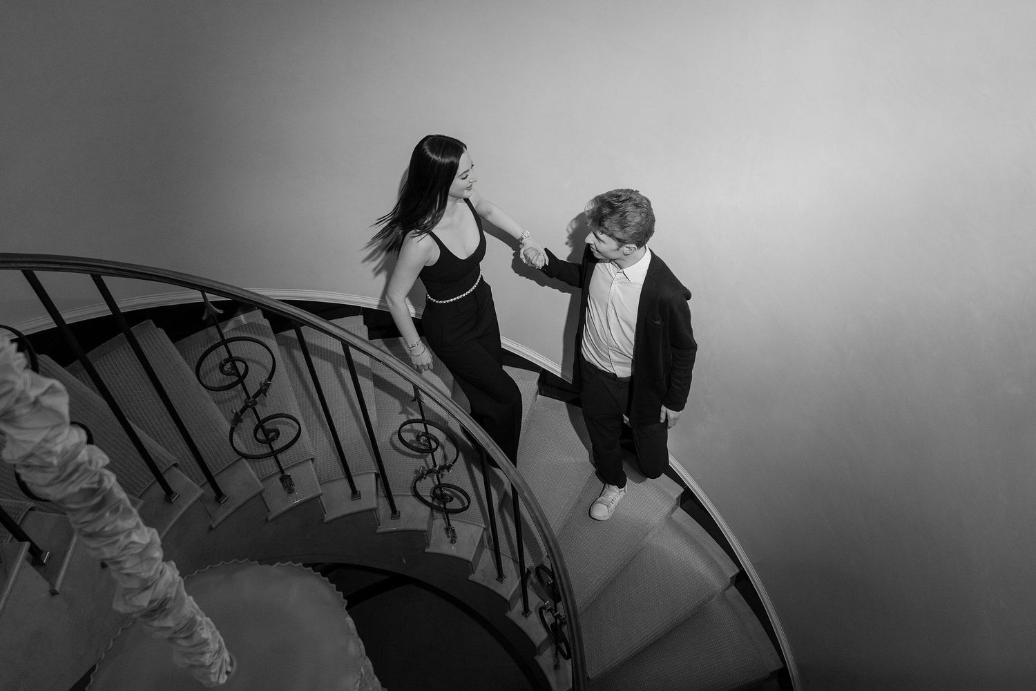 A smiling bride in a white lace dress embraces a groom in a black suit against a neutral background.