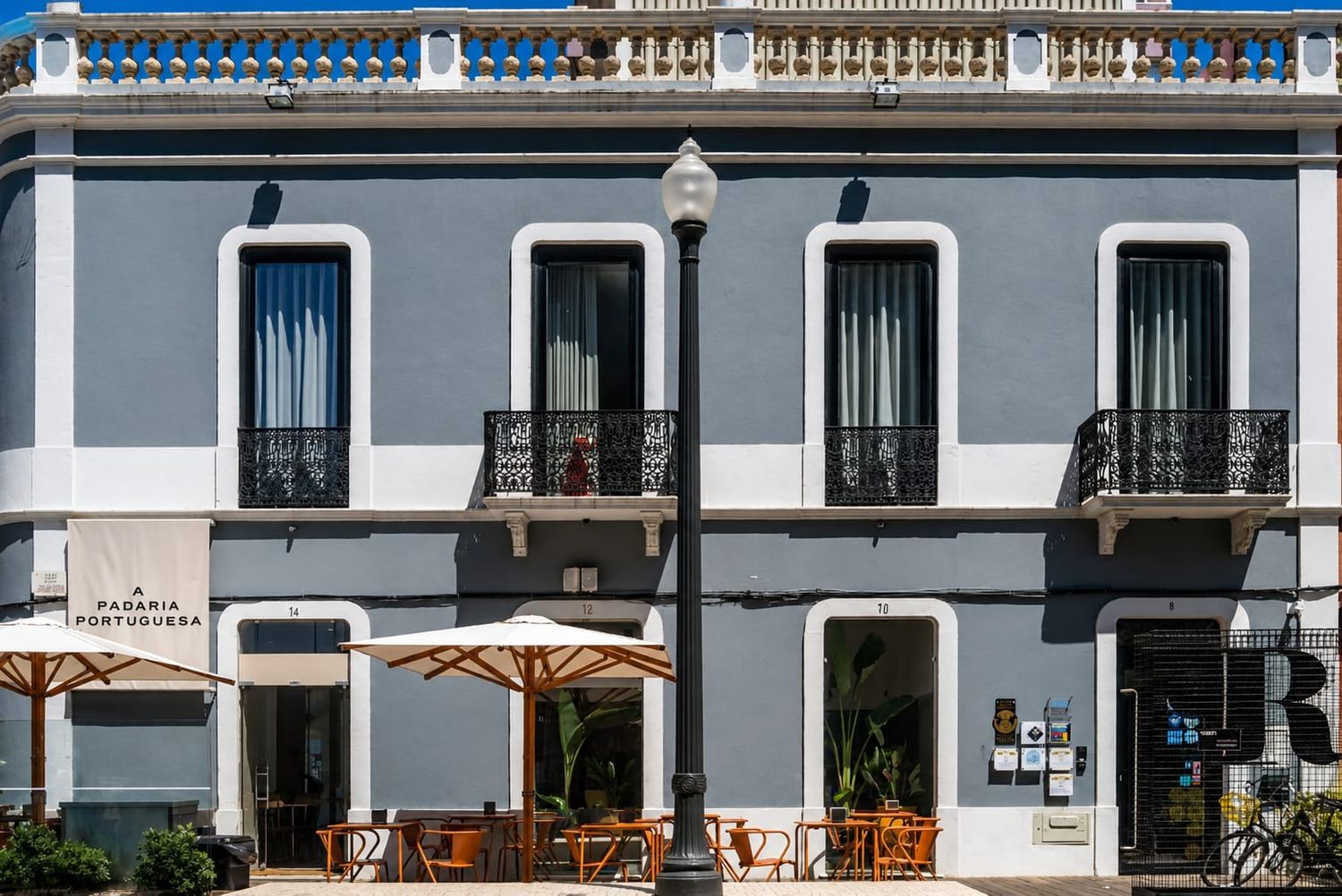 Historic gray colonial building with ornate balconies, outdoor cafe seating, and a street lamp in Old San Juan.