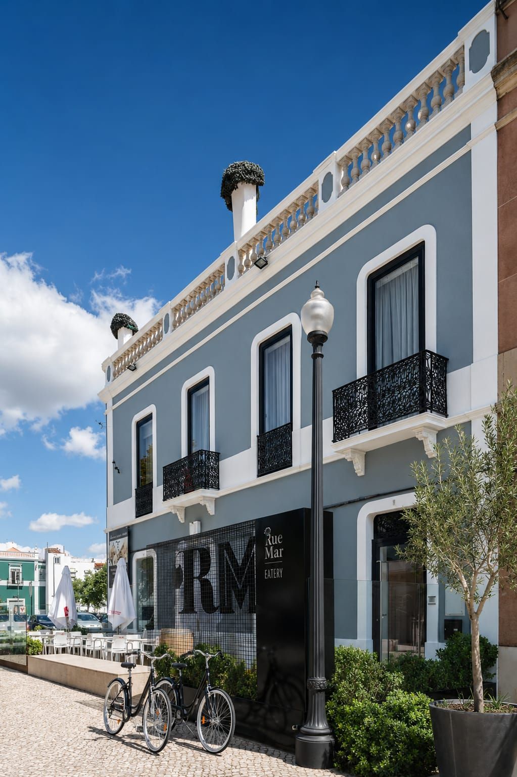 Elegant blue and white Portuguese building with wrought iron balconies, bikes parked outside RM restaurant on cobblestone street.