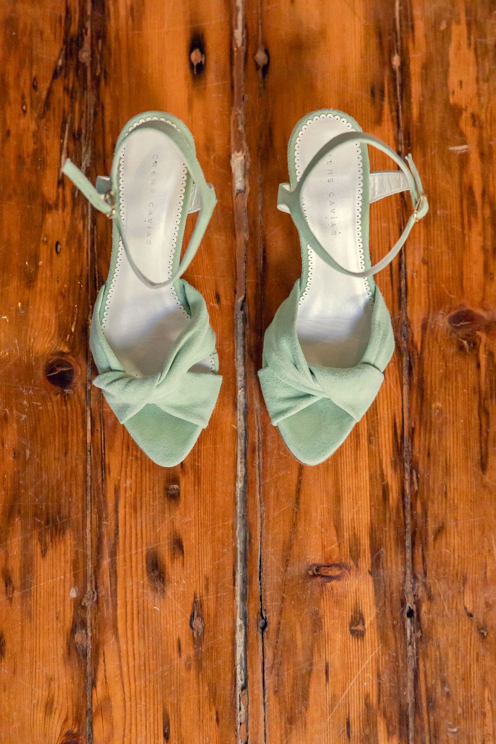 Mint green satin heeled sandals with bow detail and ankle straps displayed on rustic wooden surface.