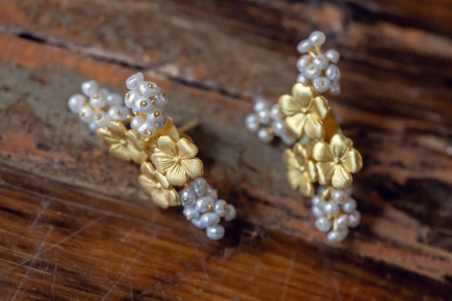 Gold flower and pearl cluster earrings displayed on rustic wooden surface.