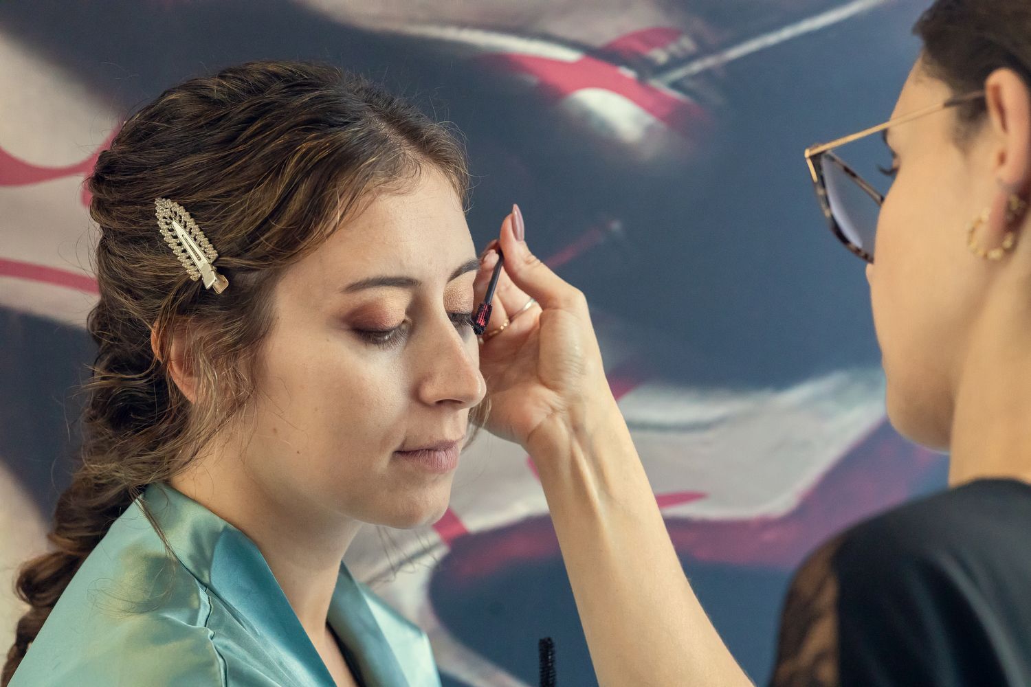 A makeup artist applies eye makeup to a young woman with a hair clip during a professional beauty session.