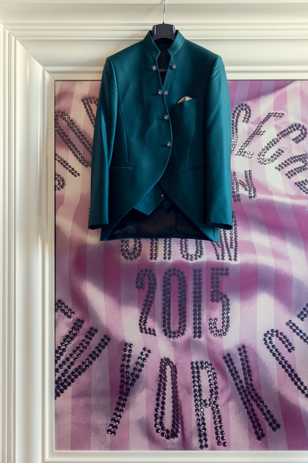 Teal mandarin collar jacket on hanger displayed against a pink rhinestone 2015 New York decorative background.