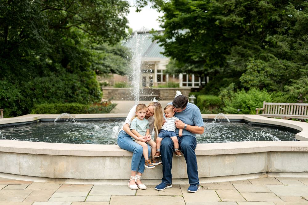 Family of four sharing a tender moment seated by a garden fountain.