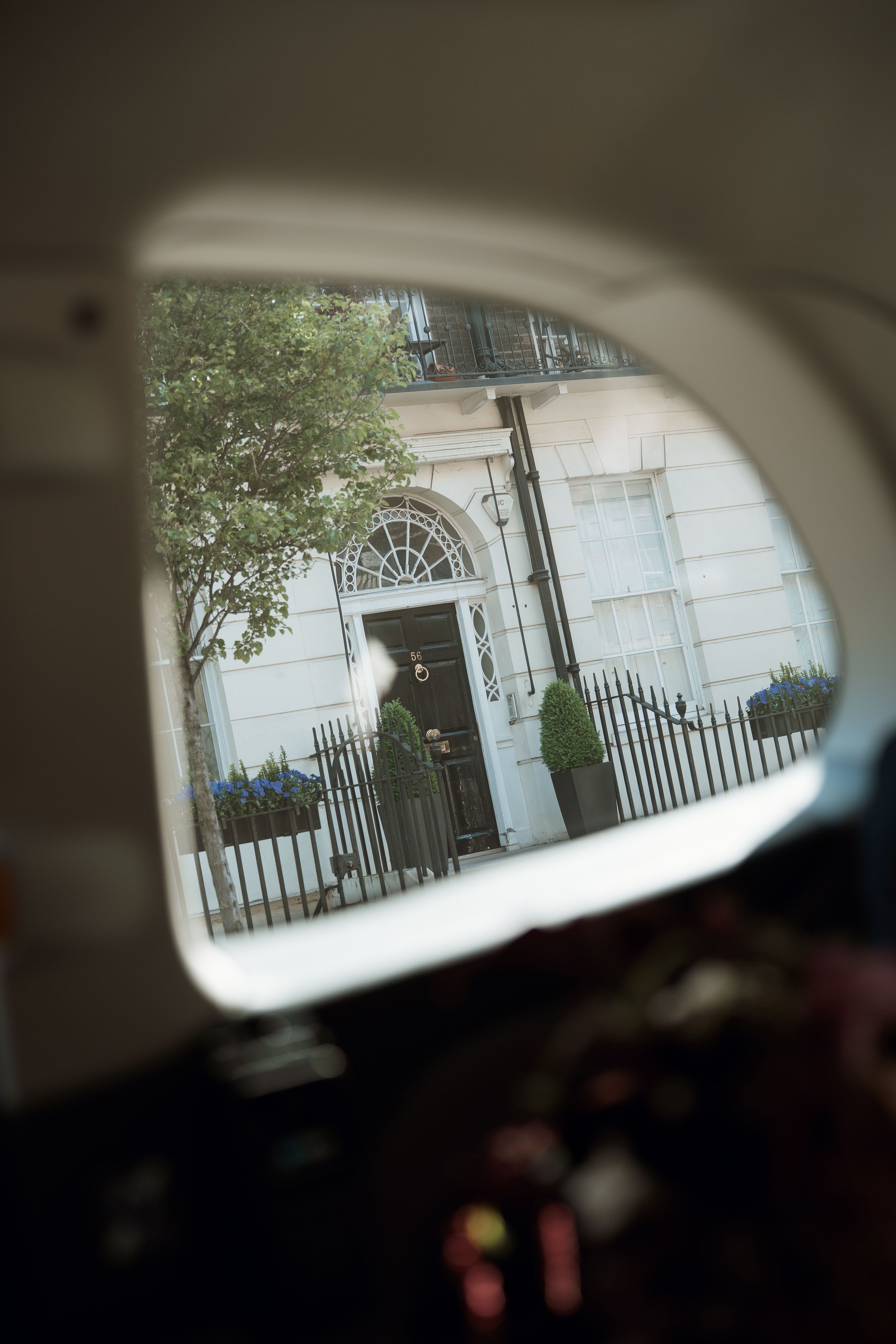 View through a car window of an elegant Georgian townhouse with black iron railings and a fanlight doorway in London.