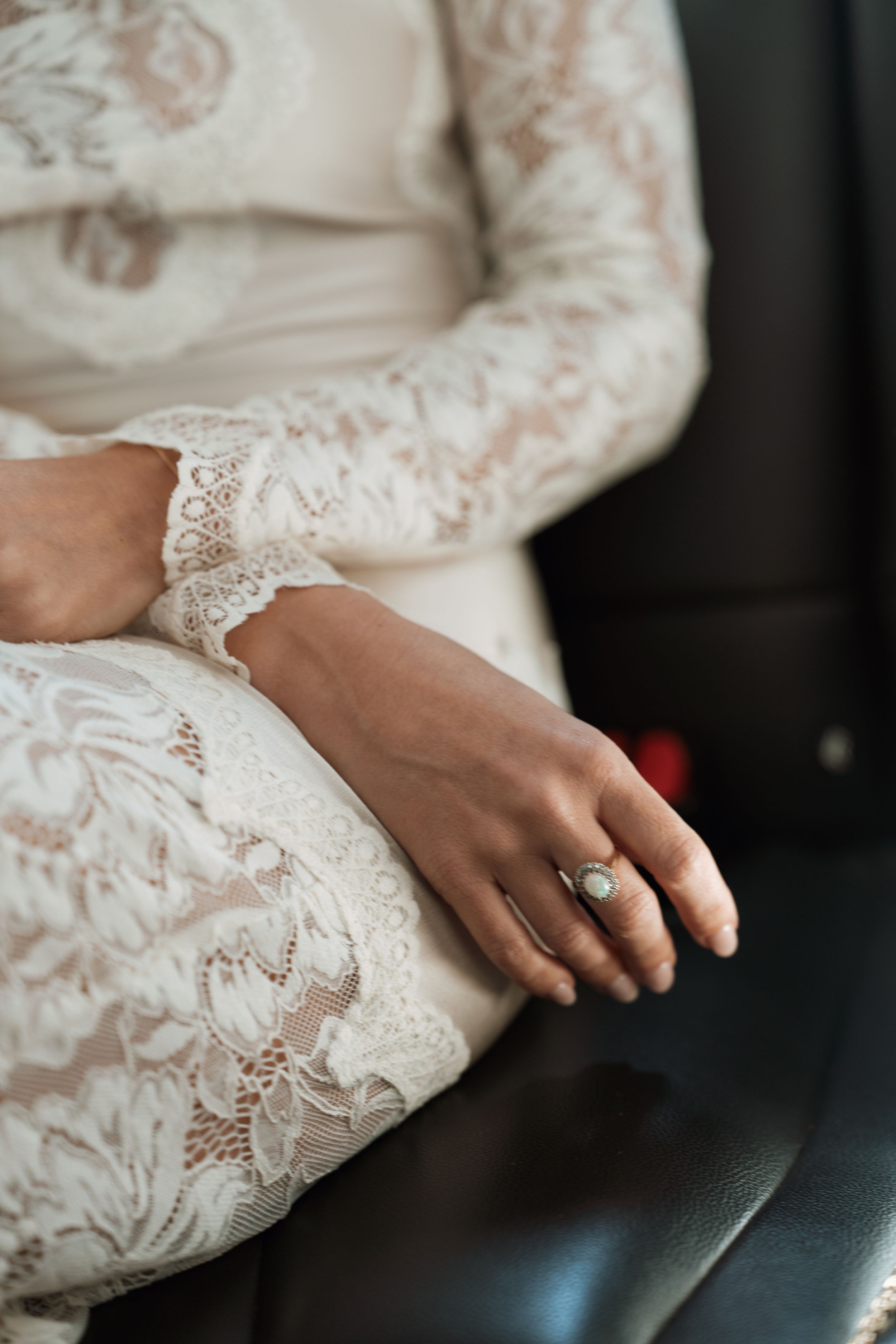 Close-up of a bride in a white lace dress sitting in a car, wearing an elegant silver ring on her finger.