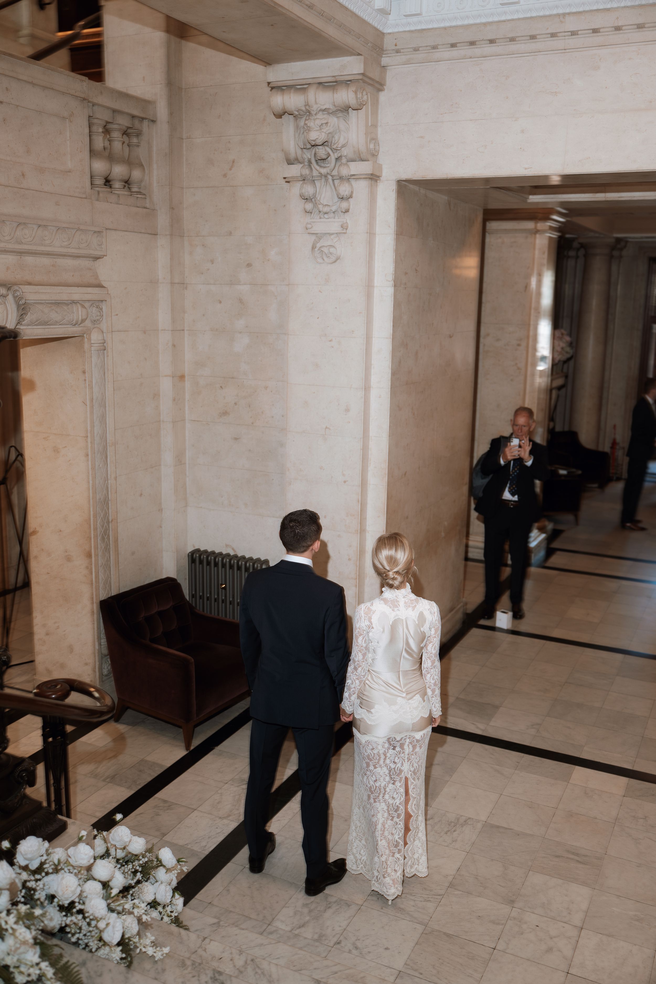 Bride and groom walking hand in hand through an elegant marble hall during their wedding ceremony.