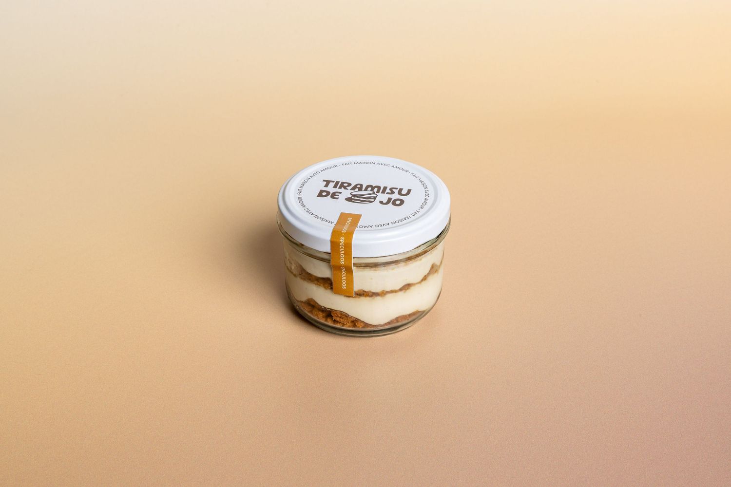 Tiramisu de Jo dessert in a small glass jar with layered cream and biscuit on a beige background.
