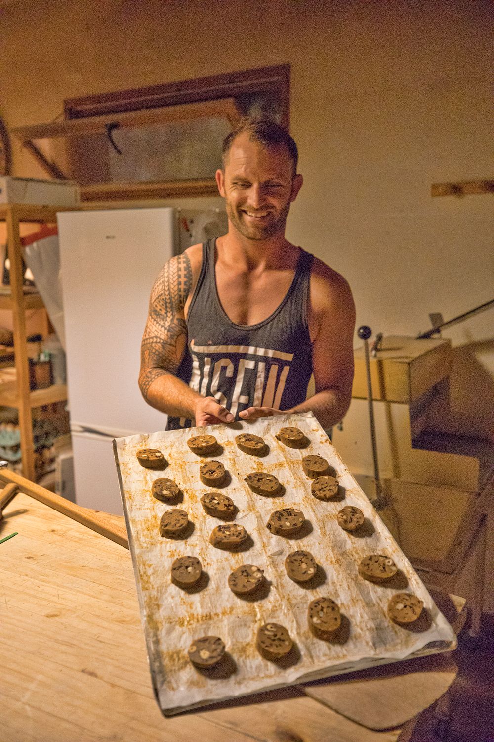 Smiling tattooed baker proudly displaying a tray of freshly baked cookies.