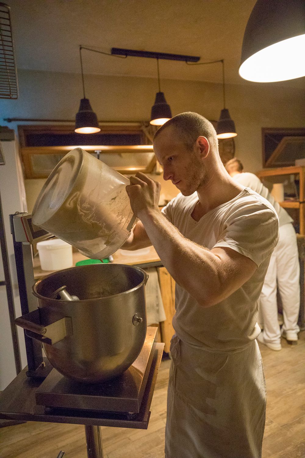 Male baker pouring ingredients into a commercial stand mixer in a professional bakery.