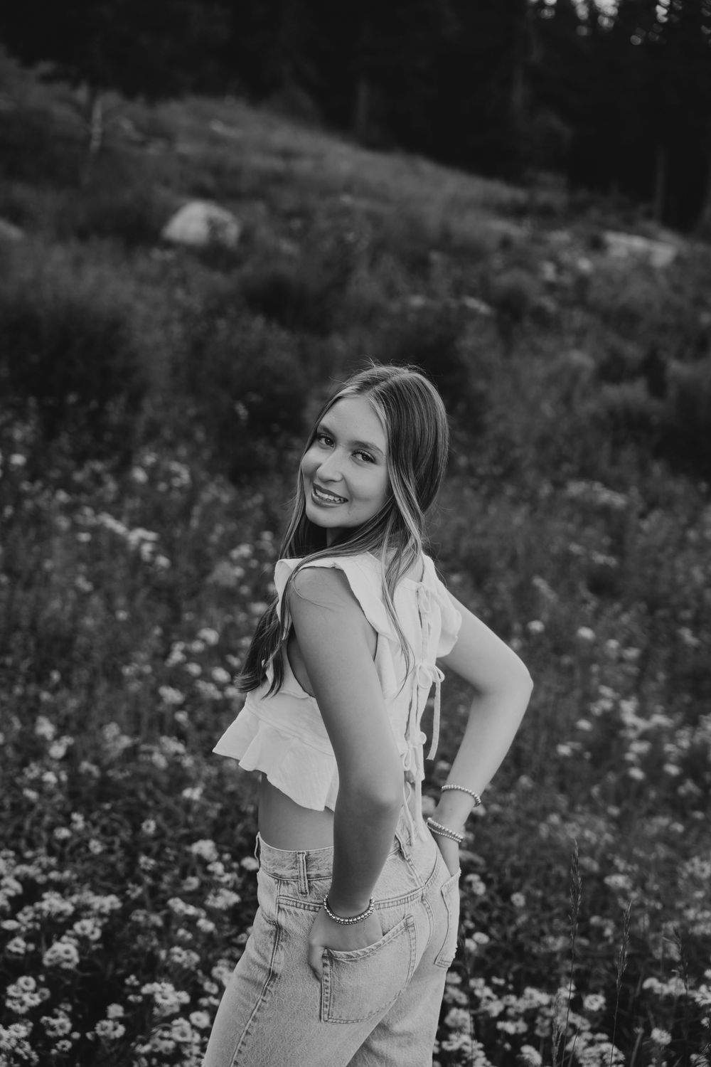 Young woman smiling in a wildflower meadow, wearing a white top and jeans, black and white portrait photo.