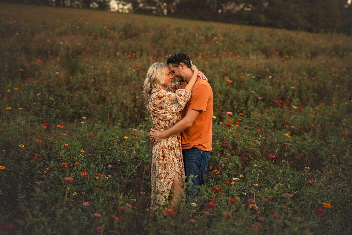 Couple embracing romantically in a vibrant wildflower field at golden hour, wearing floral dress and orange shirt.