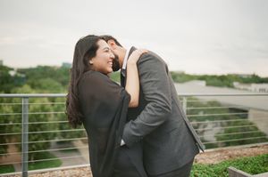 Couple embracing and laughing on a rooftop terrace, woman in black wrap and man in gray suit.