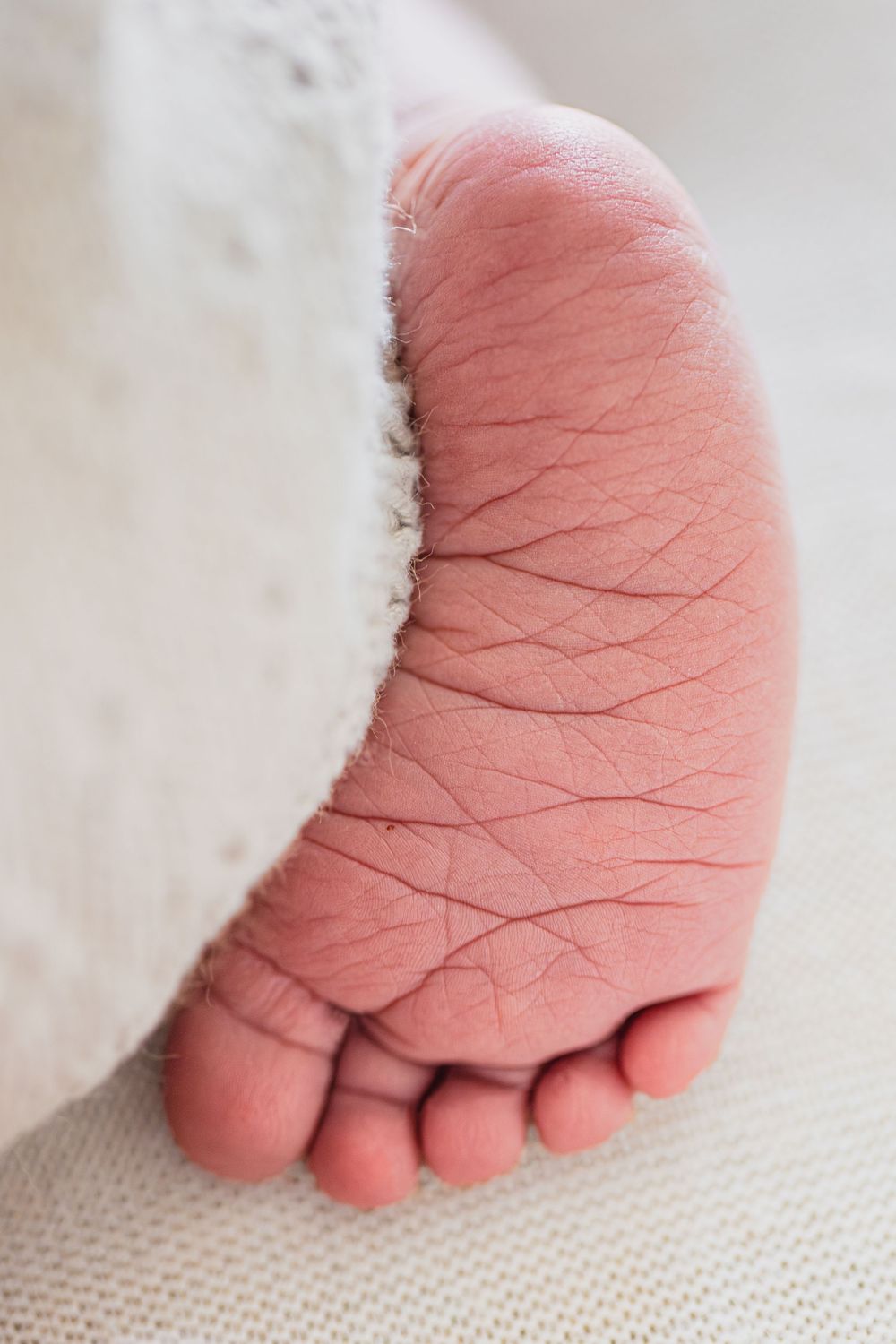 Extreme close-up of a newborn baby's soft wrinkled foot peeking out from white blanket.