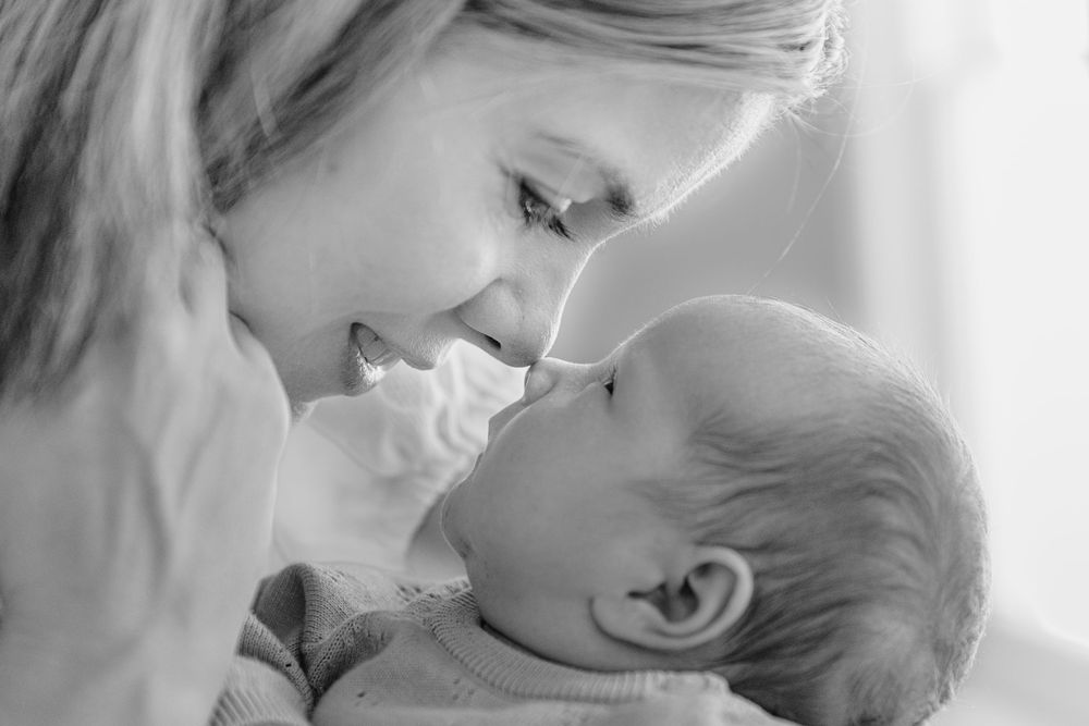 A mother smiles tenderly at her newborn baby in a heartwarming black and white portrait.