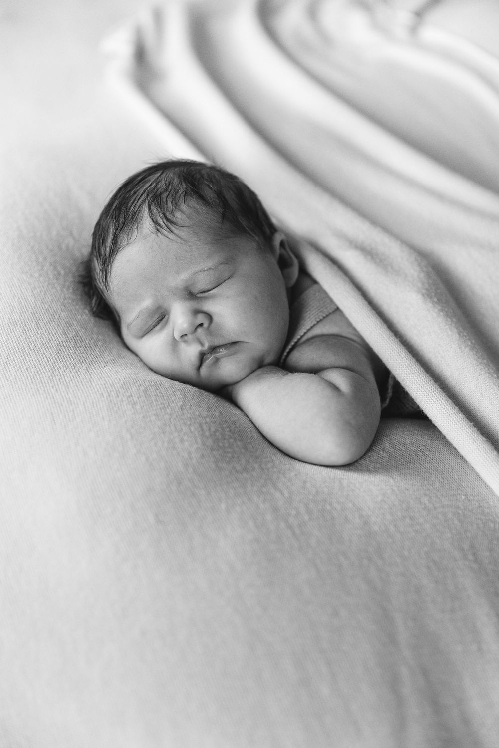 Black and white photo of a sleeping newborn baby wrapped snugly in a soft blanket.