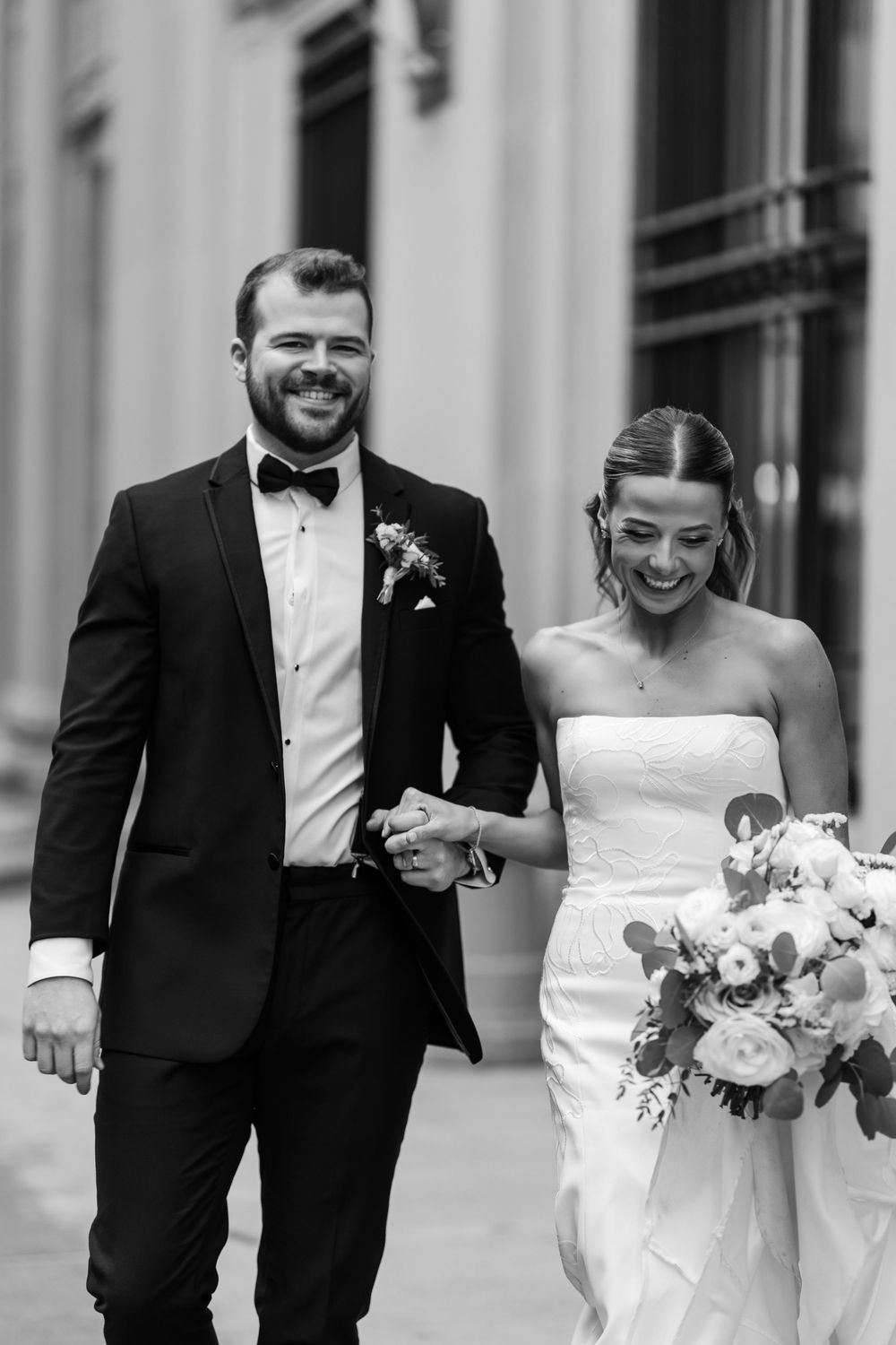 Happy bride and groom walking hand in hand in black and white wedding portrait.